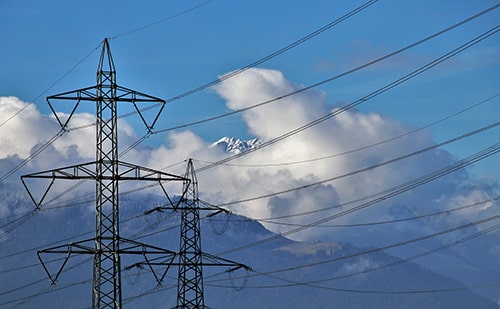 Strommasten in Landschaft mit Schneebergen und Wolken